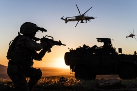 Battlefield with a soldier, armored vehicle and flying helicopters at sunset