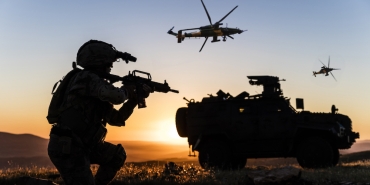 Battlefield with a soldier, armored vehicle and flying helicopters at sunset